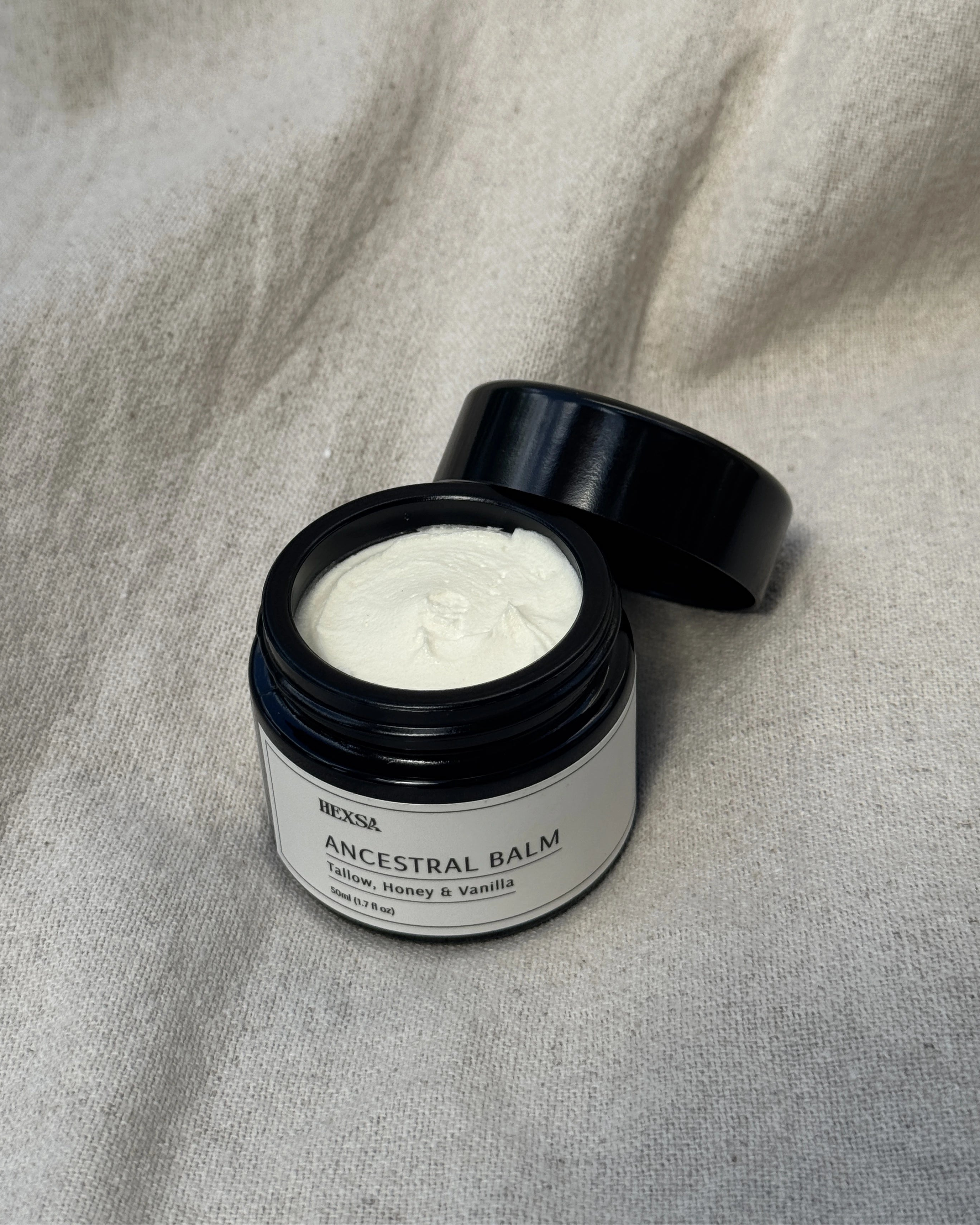 Open jar of 'Ancestral Balm' on a textured beige fabric background